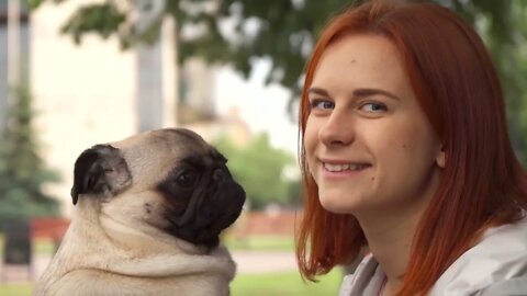 Girl trying to kiss her pug and looking at camera