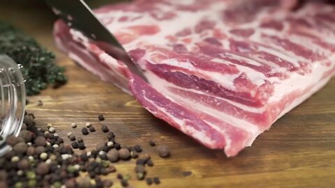 Chef cuts pieces of raw bacon by sharp knife on the wooden board, cooking meat, meals with meat prod