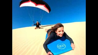 Sandboarder takes on paraglider in race down dune