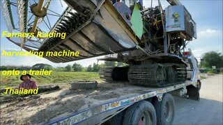 Thai farmers loading a harvesting machine onto a trailer in Thailand