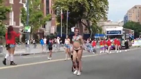 Man bearing naked breasts holding a sex work sign twerks as children look on from the crowd