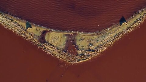 Pink sea waves splashing sandy beach at red water surface at summer. Top view salt mineral island a