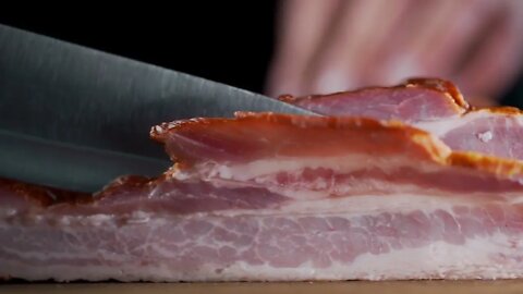 Chef cuts pieces of smoked bacon by sharp knife on the wooden board, cooking meat, meals with meat p