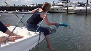 A Woman Struggles To Break A Champagne Bottle On The Side OF A Boat