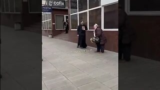 Undeva în Rusia, un preot îi trage un șut unei bătrâne pentru că vinde flori în aria lui de cerșit