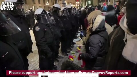 CANADIAN PROTESTORS PUT FLOWERS ON THE GROUND IN FRONT OF RIOT POLICE