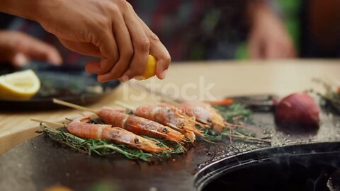 Closeup prawns browning with herbs on bbq grill on backyard. Unknown person squeezing juicy lemon