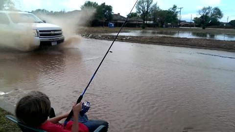 "A Young Boy Fishes on A Water-Covered Road"