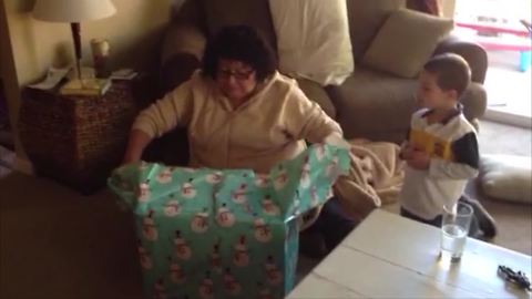 "Christmas Prank: A woman unwraps a box indoors and her son jumps out of it"