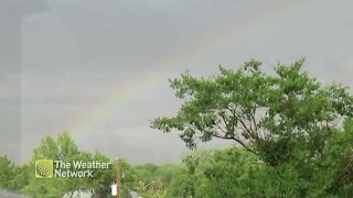 Faint rainbow stretches across the sky during a summer rain