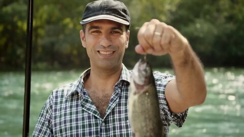 Mid adult fisherman on holidays on river, relaxing and fishing trout, showing fish to the camera