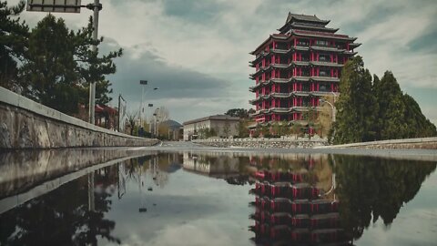 Gentle rain hitting a large puddle on a road in front of a red and brown pagoda