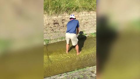 A Man Tries To Hit A Golf Ball In Shallow Water But Fails