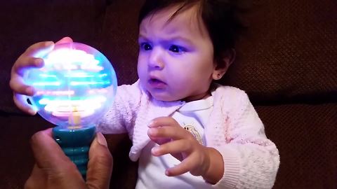 A Baby Girl Stares At A Spinning Ball Of Light And Furrows Her Brow