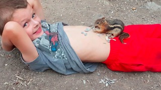 A Little Boy Lets A Squirrel Eat Sunflower Seeds Off Of His Belly