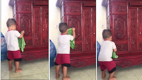The baby uses a towel to wipe the wooden cabinet