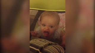 "A Baby Girl Stands In Her Playpen And Makes Funny Faces"