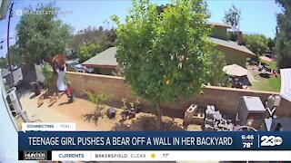 Teenage girl pushes a bear off a wall in backyard