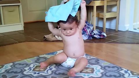 Persistent baby repeatedly puts pants on his head