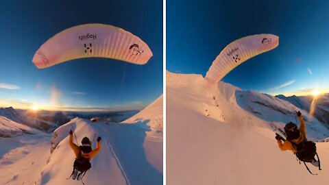 Paraglider flies and skis over golden hour mountains