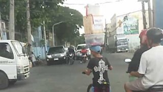 Jovem vendedor transporta caixas na cabeça enquanto anda de bicicleta