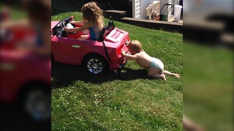 A Baby Boy Pushes A Big Toy Car For His Sister