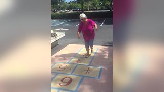 A Senior Woman Tries To Play Hopscotch