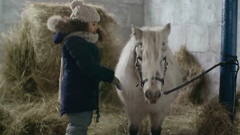 Little African American girl with curly hair gently hugging pony in barn