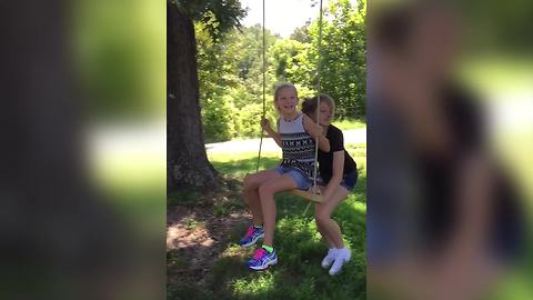 A Young Girl Swings On A Tree Swing And Knocks Over A Friend