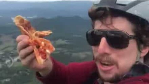 Amante de pizza come fatia enquanto faz parapente