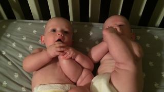 "Twin Baby Boys Lie in A Crib and One Chews the Others Foot"