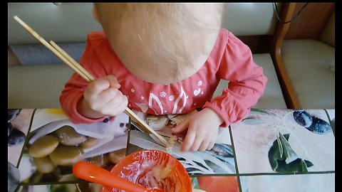Funny baby trying to learn to eat with chopsticks.
