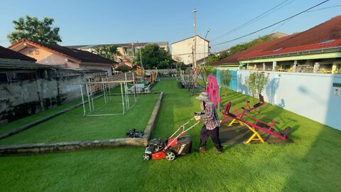 Cutting grass at children's playground in Thailand