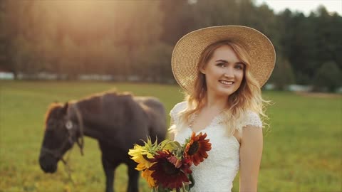 Rear view of a young bride standing near a horse. Turning around, smiling, looking down