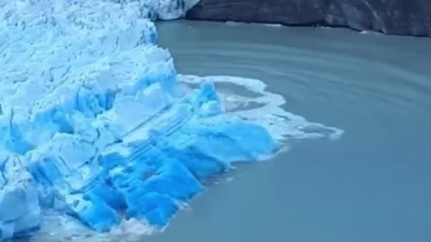 Rare sighting of the deep blue underside of a glacier during a collapse caused by glacier caving