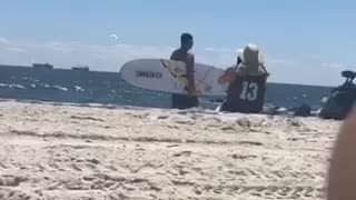 13 jersey guy taking picture of friend holding surfboard on beach
