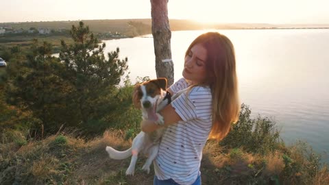 Young attractive woman playing with a dog Jack Russell in the meadow at sunset with sea background