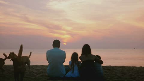 Beautiful back view shot of happy family sit together watching amazing sunset on epic sea beach