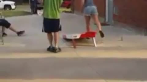 Skateboarder trips in front of guys playing cornhole