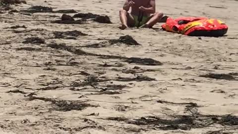 Man on beach next to orange raft has shake weight