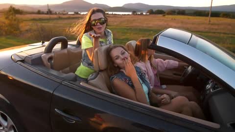 Happy girls traveling in a convertible car at sunset