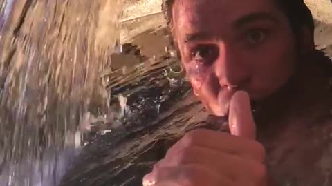 Guy swimming in water and opens mouth near waterwall