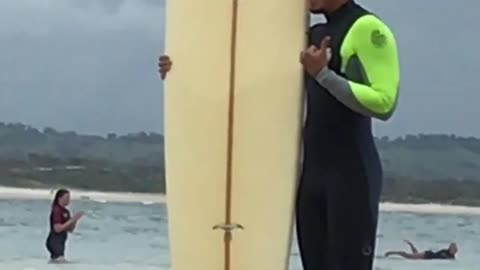 Guy in green wetsuit posing next to board