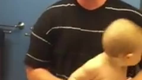Baby adorably flexes muscles with dad.