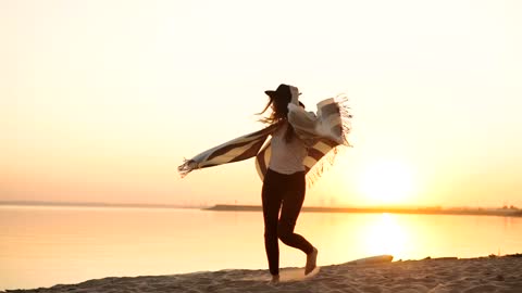 Stylish millennial woman spins on beach at sunset