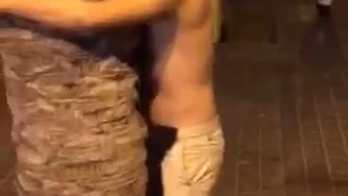 Shirtless guy licks and hugs tree outside at night