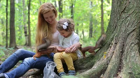 A cute little girl and her mom feed the red squirrels in the Park