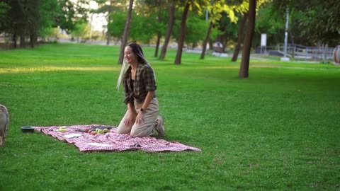 Woman with dreadlocks playing with her dog on grass, having picnic outdoors in the green park alone