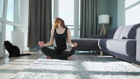 Young caucasian woman in black jumpsuit doing yoga at home to develop flexibility and balance
