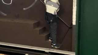 Guy graffiti tags a subway wall behind subway train tracks